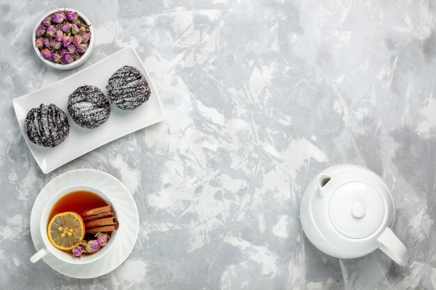 Вид сверху вкусные маленькие пирожные с глазурью и чашкой чая на белом столе чайный бисквитный торт испечь сахарный сладкий пирог