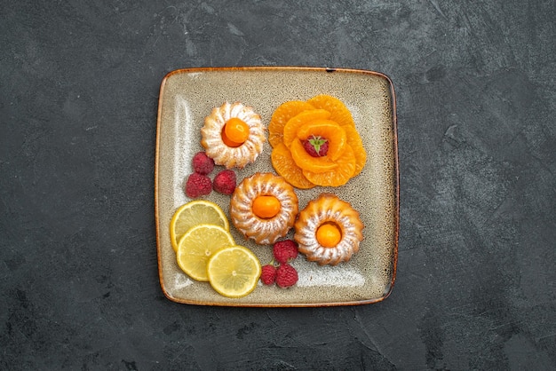 Вид сверху вкусные маленькие пирожные с дольками лимона и мандаринами на темном фоне фруктовое печенье сладкое чайное печенье