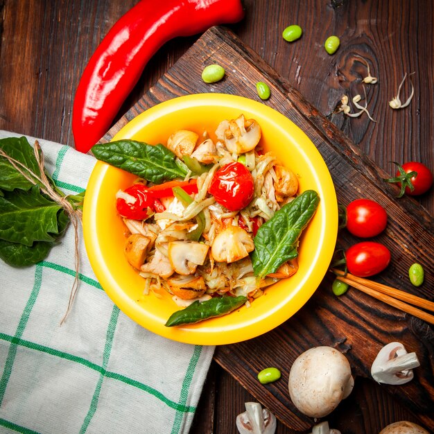 Top view delicious meal in yellow plate with red pepper, tomatoes on wood, cloth and dark wooden background.