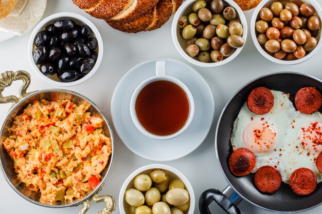 Top view delicious meals in pan and pot with pickles, a cup of tea on white surface