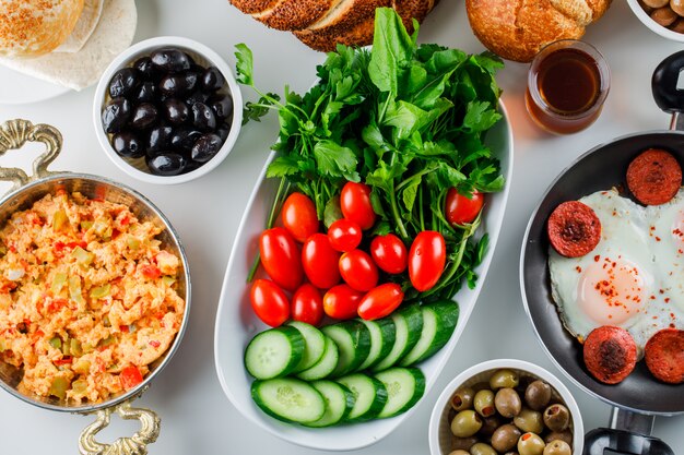 Top view delicious meals in pan and pot with salad, pickles, turkish bagel, a cup of tea on white surface