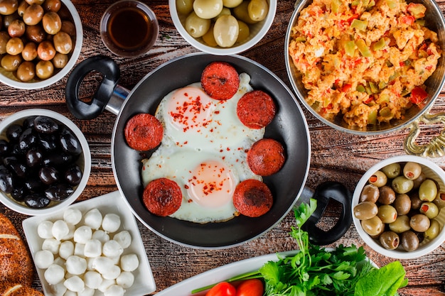 Top view delicious meals in a pot and pan with pickles in bowls on wooden surface