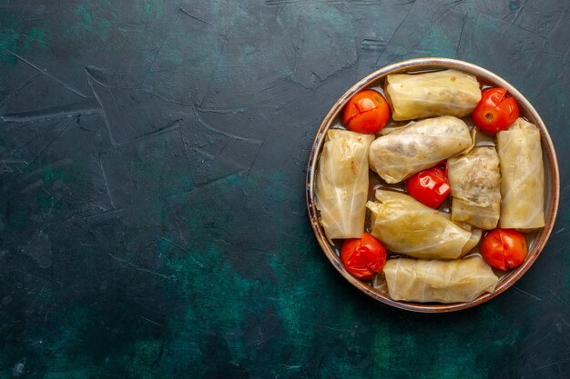 Top view delicious meat meal rolled inside cabbage with tomatoes on the dark blue desk meat food dinner calorie vegetable cooking