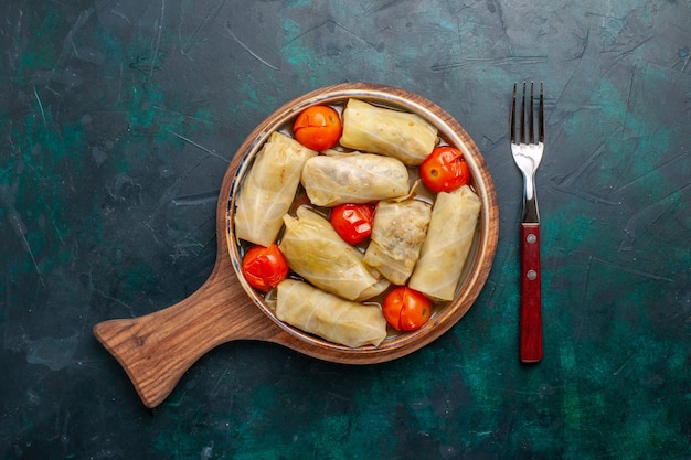 Top view delicious meat meal rolled inside cabbage with tomatoes on dark-blue floor meat food dinner calories vegetable dish cooking