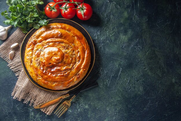 Top view of delicious meat pie with ingredients on dark surface