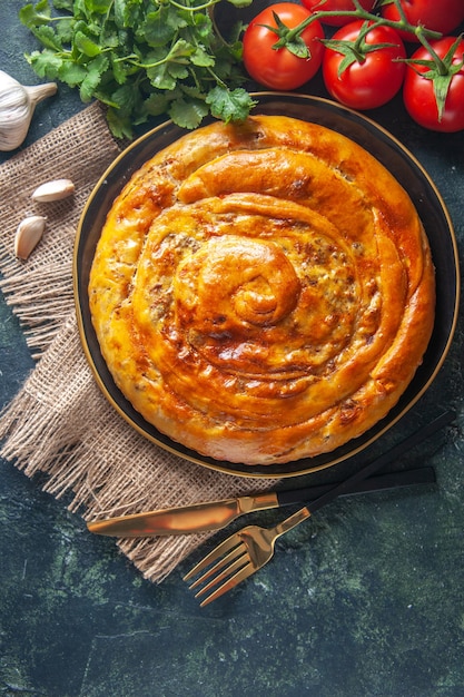 Top view of delicious meat pie with ingredients on dark surface