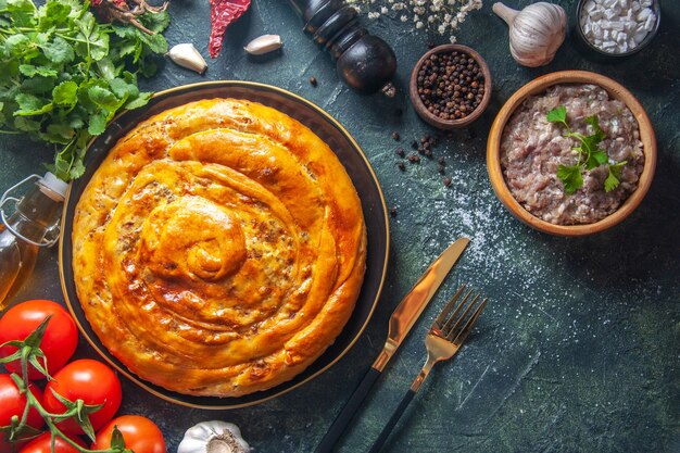 Top view of delicious meat pie with ingredients on dark surface