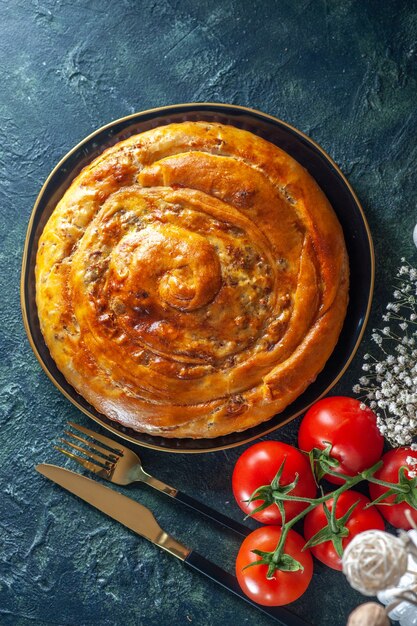 Top view of delicious meat pie with ingredients on dark surface