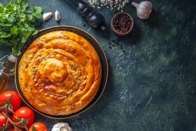 Top view of delicious meat pie with ingredients on dark surface