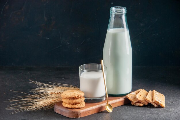 Вид сверху вкусного молока в стакане и бутылки печенья, сложенного золотой ложкой на шипах на деревянном подносе на темной поверхности