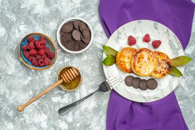 Top view delicious muffins with choco biscuits honey and raspberries on light background