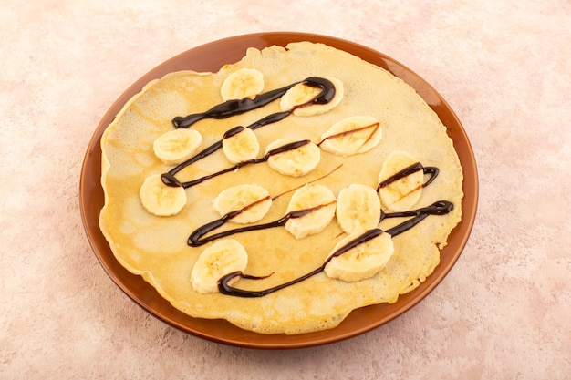 Free photo a top view delicious pancakes designed with chocolate and bananas inside brown round plate on the pink desk food meal dessert pastry