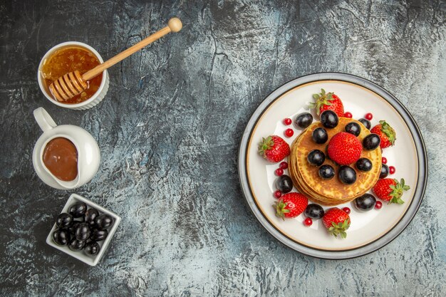 Top view delicious pancakes with honey and fruits on light desk fruit cake sweet