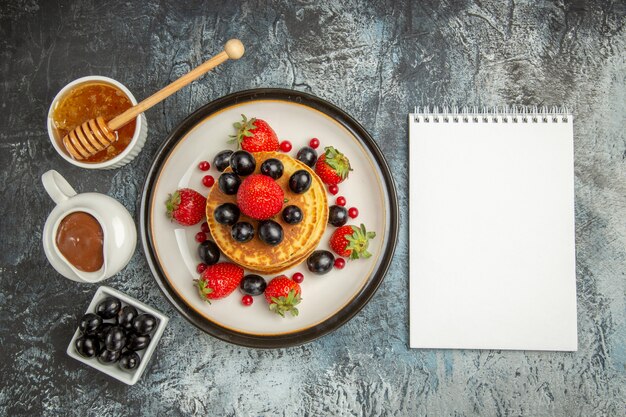 Top view delicious pancakes with honey and fruits on a light surface fruit cake sweet