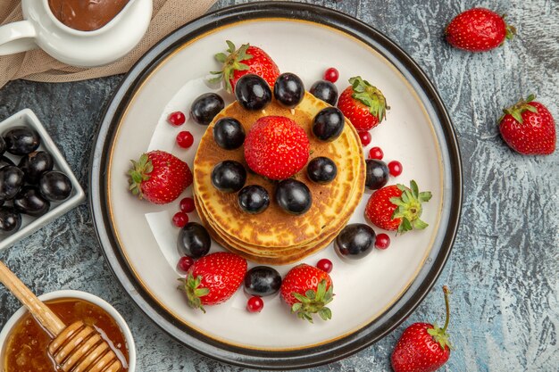 Top view delicious pancakes with honey and fruits on light surface sweet fruit cake