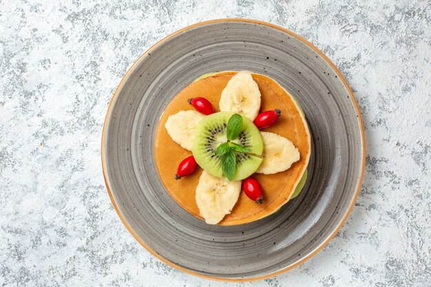 Top view delicious pancakes with sliced fruits inside plate on white surface fruit sweet dessert sugar cake breakfast color