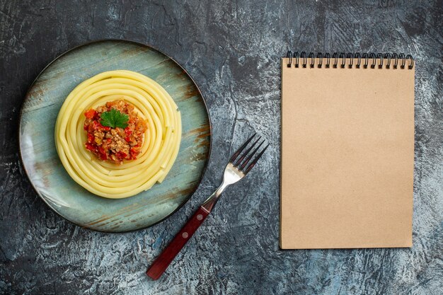 저녁 식사와 포크, 닫힌 노트북으로 토마토와 고기를 곁들인 파란색 접시에 있는 맛있는 파스타 식사의 최고 전망