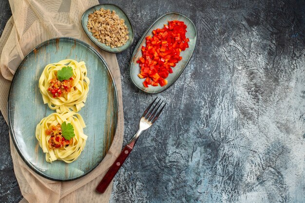 파란색 접시에 있는 맛있는 파스타 식사의 최고 전망은 토마토와 고기를 곁들인 저녁 식사로 황갈색 타월의 재료로 제공됩니다.