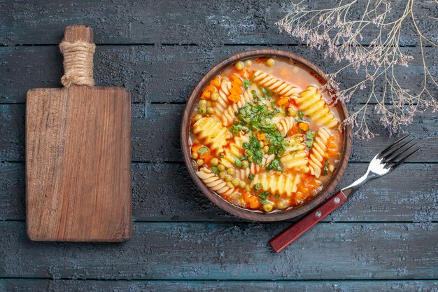 Вид сверху вкусный суп-паста из спиральной итальянской пасты с зеленью на темно-синем столе обеденное блюдо итальянская паста-суп соус