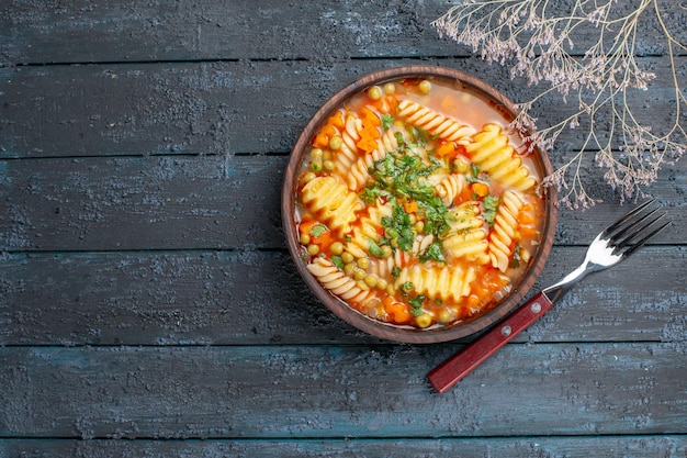 Вид сверху вкусный суп-паста из спиральной итальянской пасты с зеленью на темно-синем столе обеденное блюдо итальянская паста-суп соус