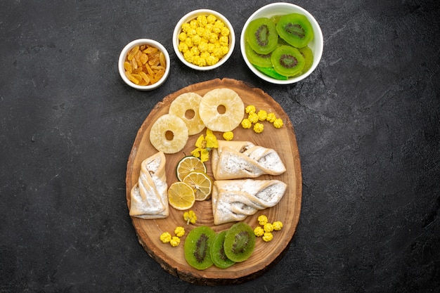 Free photo top view delicious pastries with dried pineapple rings and kiwis on dark grey desk