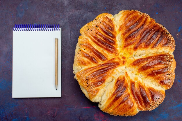 トップビューおいしいペストリー焼きパンは、暗い背景にメモ帳でペストリーを形成しました。