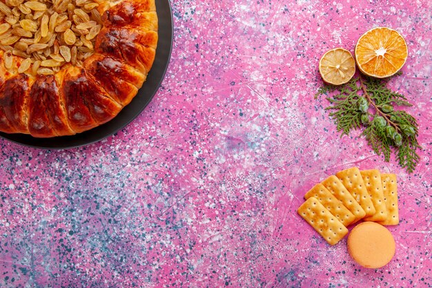 Top view delicious pastry cake with raisins and crackers on pink desk