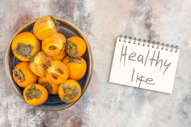 Top view delicious persimmons in a bowl healthy life written on notepad on nude background