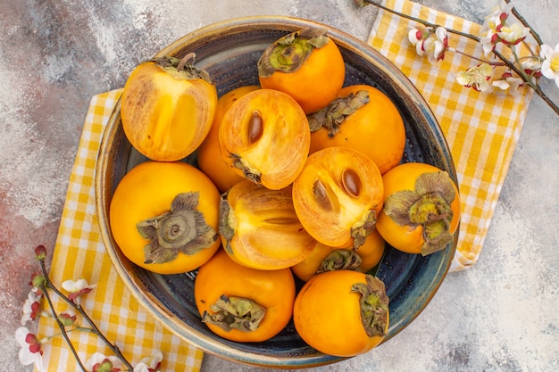 Top view delicious persimmons in a bowl yellow kitchen towel apricot blossom branch on nude background