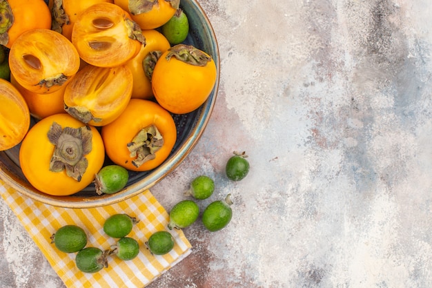 Top view delicious persimmons in a bowl yellow kitchen towel feykhoas on nude background