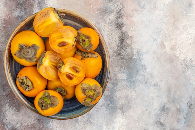 Free photo top view delicious persimmons cut persimmons in round wood box on nude background