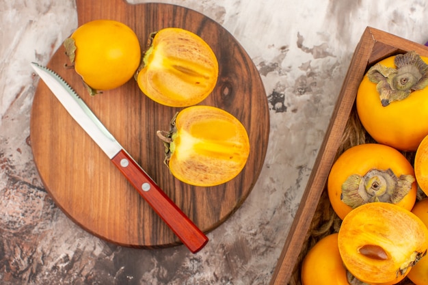 Top view delicious persimmons a knife on cutting board persimmons box on nude background