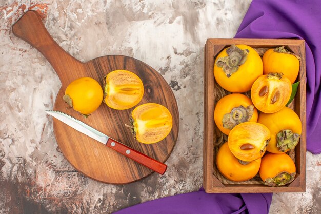 Top view delicious persimmons a knife on cutting board persimmons box purple shawl on nude background