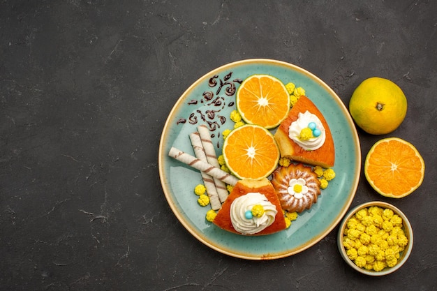 Top view delicious pie slices with pipe cookies and fresh sliced tangerines on dark background fruit cake pie sweet biscuit