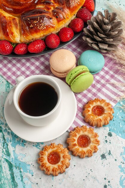 Вид сверху вкусный пирог со свежими красными клубничными макаронами и чашкой чая на синей поверхности
