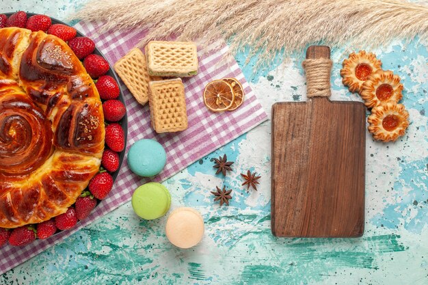 Top view delicious pie with macarons waffles and fresh red strawberries on blue surface