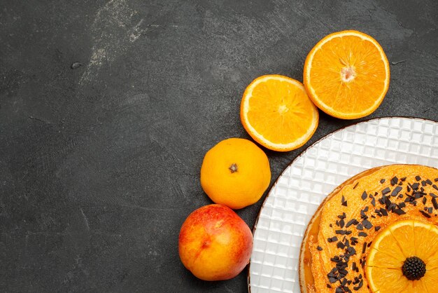 暗い表面にオレンジスライスが入ったトップビューのおいしいパイフルーツデザートパイケーキビスケットティー