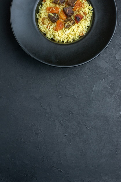 Top view delicious pilaf cooked rice with dried apricots and meat slices inside plate on dark surface