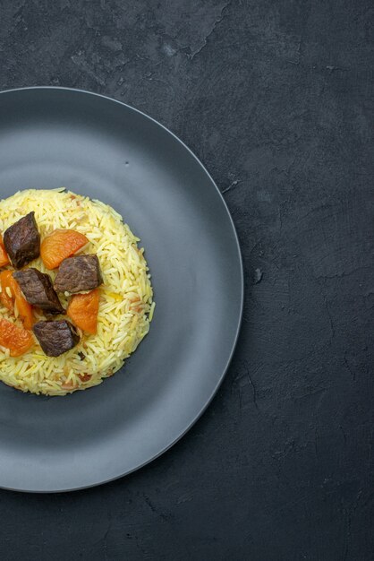 Top view delicious pilaf cooked rice with dried apricots and meat slices inside plate on dark surface