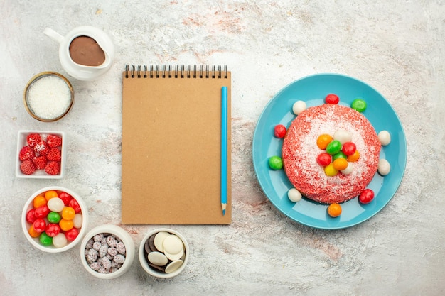 Top view delicious pink cake with colorful candies on light white surface color dessert cake rainbow candy