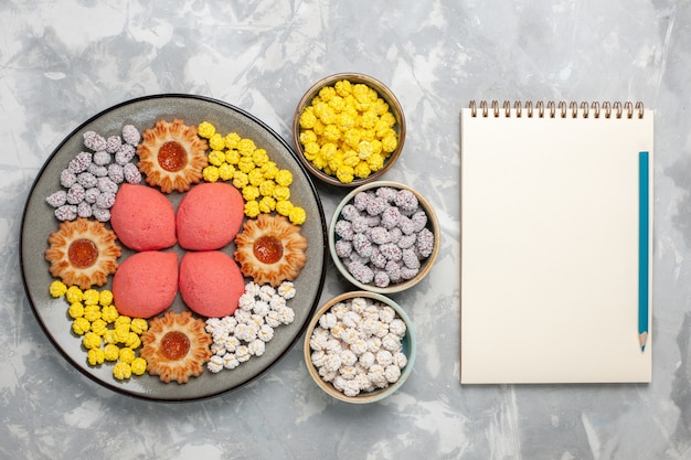 Foto gratuita vista dall'alto deliziose torte rosa con caramelle e biscotti sulla superficie bianca torta dolce biscotto torta di tè biscotti