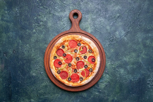 Top view of delicious pizza on wooden cutting board on dark blue surface
