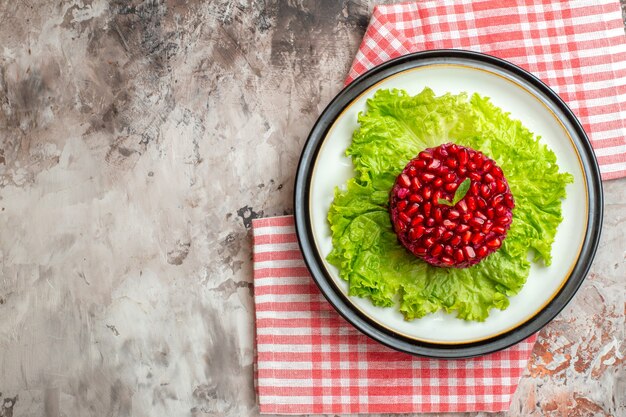 Вид сверху вкусный гранатовый салат круглой формы на зеленом салате на светлом фоне