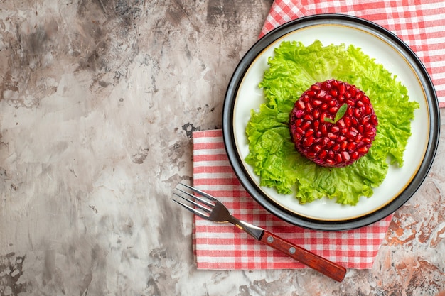 Вид сверху вкусный гранатовый салат круглой формы на зеленом салате на светлом фоне