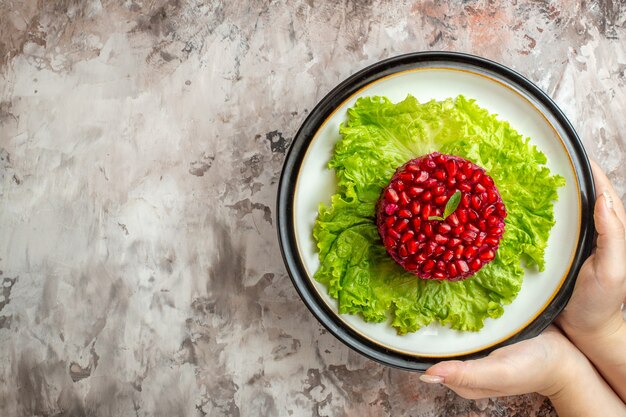 Вид сверху вкусный гранатовый салат круглой формы на зеленом салате на светлом фоне