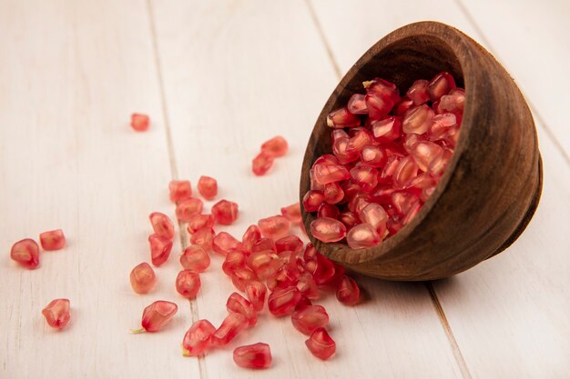 Top view of delicious pomegranate seeds falling out of a wooden bowl with seeds isolated on a white wooden surface