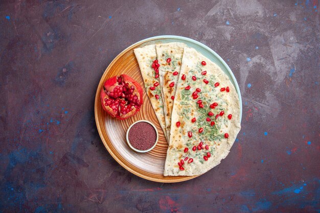 Top view delicious qutabs cooked dough pieces with greens and pomegranates on a dark surface dough meal dinner cooking dish