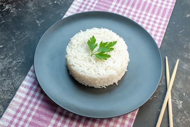보라색 벗겨진 수건에 검은 접시에 녹색과 어두운 배경에 나무 젓가락으로 제공되는 맛있는 쌀 식사의 상위 뷰