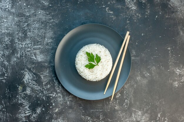 Вид сверху вкусной рисовой еды, подаваемой с зеленью и палочками для еды на черной тарелке на темном фоне
