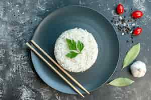 Free photo top view of delicious rice meal served with green and chopsticks on a black plate peppers garlic tomatoes on dark background